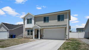 View of front of property with stone siding, driveway, an attached garage, and a gate