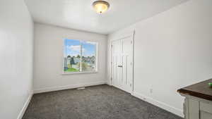 Unfurnished bedroom with dark carpet, baseboards, and a closet