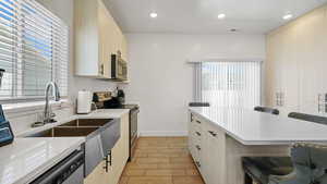 Kitchen featuring stainless steel appliances, light countertops, a kitchen bar, recessed lighting, and baseboards