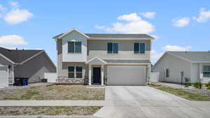 View of front of house with concrete driveway, stone siding, an attached garage, and a shingled roof