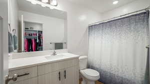 Bathroom with toilet, vanity, a walk in closet, and a shower with curtain