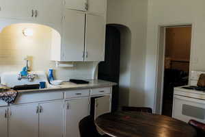 Kitchen with white range oven, decorative backsplash, light countertops, white cabinetry, and arched walkways