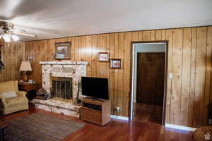 Living area with a ceiling fan, a fireplace, wood finished floors, wood walls, and baseboards