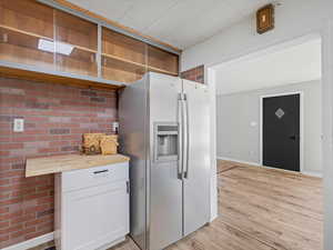 Kitchen featuring stainless steel fridge with ice dispenser, wooden counters, light wood-type flooring, baseboards, and open shelves