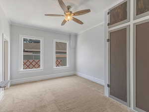 Carpeted spare room with crown molding, baseboards, and a ceiling fan