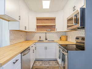 Kitchen featuring stainless steel appliances, butcher block countertops, a sink, decorative backsplash, and white cabinets