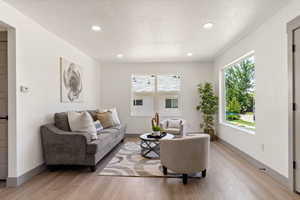 Living room with light wood-type flooring, recessed lighting, baseboards, and a textured ceiling