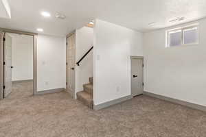 Basement featuring carpet flooring, stairway, baseboards, recessed lighting, and a textured ceiling