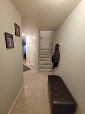 Corridor with stairs, light tile patterned flooring, a textured ceiling, and baseboards