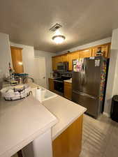 Kitchen featuring stainless steel appliances, brown cabinets, light countertops, a textured ceiling, and a sink