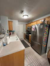 Kitchen featuring appliances with stainless steel finishes, a sink, light countertops, brown cabinets, and a textured ceiling