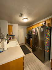 Kitchen featuring appliances with stainless steel finishes, a sink, brown cabinetry, light countertops, and a textured ceiling