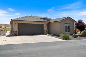 View of front of home featuring a garage, stone siding, driveway, and a tiled roof