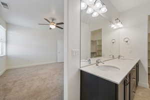 Full bath with ceiling fan, double vanity, and baseboards