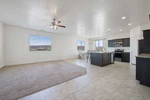 Kitchen featuring appliances with stainless steel finishes, dark cabinets, a ceiling fan, a center island with sink, and open floor plan