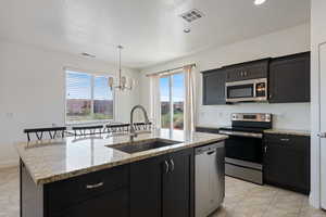 Kitchen with stainless steel appliances, a sink, a chandelier, a center island with sink, and hanging light fixtures