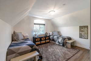 Bedroom with wood finished floors, lofted ceiling, and baseboards
