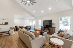 Living area with high vaulted ceiling, light wood-style floors, recessed lighting, a glass covered fireplace, and ceiling fan