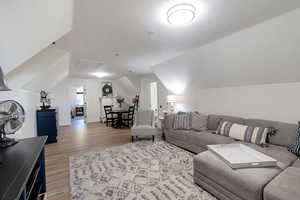 Living area with light wood finished floors, vaulted ceiling, baseboards, and attic access