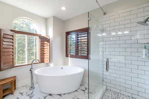 Bathroom featuring marble look tile flooring, a shower stall, a freestanding tub, recessed lighting, and baseboards