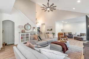 Living area featuring ceiling fan, stairway, light wood-style flooring, arched walkways, and high vaulted ceiling