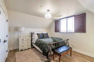 Bedroom featuring light wood-type flooring, baseboards, vaulted ceiling, and a closet