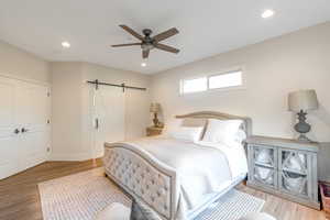 Bedroom featuring a barn door, recessed lighting, light wood finished floors, a ceiling fan, and baseboards