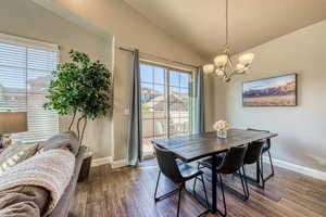 Dining room featuring healthy amount of natural light, baseboards, a chandelier, dark wood-style flooring, and lofted ceiling