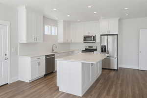 Kitchen featuring appliances with stainless steel finishes, white cabinets, dark wood finished floors, light countertops, and a kitchen island