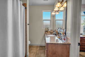 Full bath featuring double vanity, toilet, tile patterned flooring, a chandelier, and curtained shower