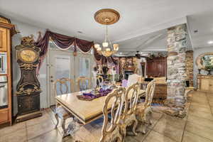 Dining space with light tile patterned floors, a chandelier, beamed ceiling, ornate columns, and a fireplace