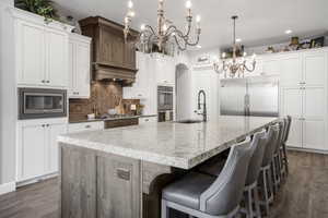 Kitchen with a chandelier, built in appliances, a sink, decorative backsplash, and a large island with sink