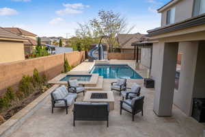 View of swimming pool featuring a water slide, a fenced backyard, an outdoor living space with a fire pit, and a patio