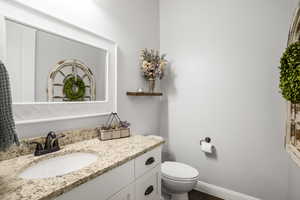 Bathroom featuring toilet, vanity, wood finished floors, and baseboards