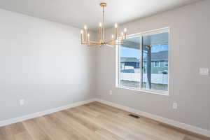 Empty room featuring a chandelier, light wood-style flooring, and baseboards