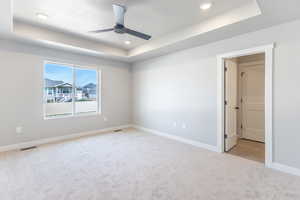 Unfurnished room with a tray ceiling, light carpet, ceiling fan, baseboards, and recessed lighting