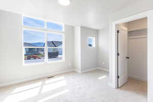 Unfurnished bedroom featuring light colored carpet, a walk in closet, and baseboards