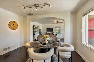 Dining space with arched walkways, dark wood-type flooring, ceiling fan, a textured ceiling, and crown molding