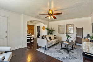 Living room featuring arched walkways, a textured ceiling, dark wood-style flooring, ceiling fan, and ornamental molding