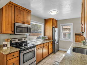 Kitchen featuring appliances with stainless steel finishes, plenty of natural light, a sink, brown cabinets, and a textured ceiling