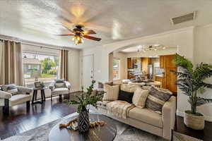 Living room with arched walkways, wood finished floors, ornamental molding, a textured ceiling, and ceiling fan