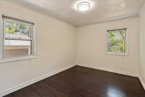 Unfurnished room featuring dark wood-style flooring, crown molding, and a textured ceiling