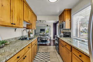 Kitchen featuring appliances with stainless steel finishes, a sink, ceiling fan, brown cabinets, and light stone counters