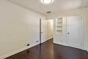 Unfurnished bedroom featuring dark wood finished floors, a textured ceiling, and ornamental molding