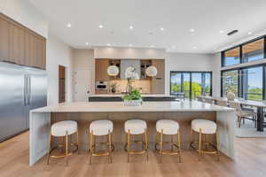 Kitchen with appliances with stainless steel finishes, a large island, modern cabinets, light countertops, and light wood finished floors
