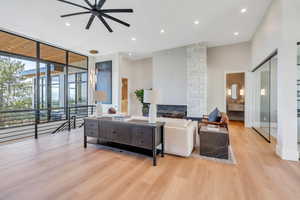 Living area with ceiling fan, light wood-type flooring, expansive windows, recessed lighting, and a fireplace
