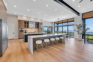 Kitchen with appliances with stainless steel finishes, a large island with sink, modern cabinets, light wood-style flooring, and light countertops