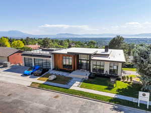 Contemporary home with a mountain view, concrete driveway, a front lawn, and a chimney