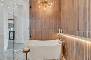 Full bath featuring a soaking tub, a chandelier, marble tiled flooring, and tile walls