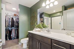 Bathroom with vanity, a shower stall, a spacious closet, toilet, and tile patterned flooring